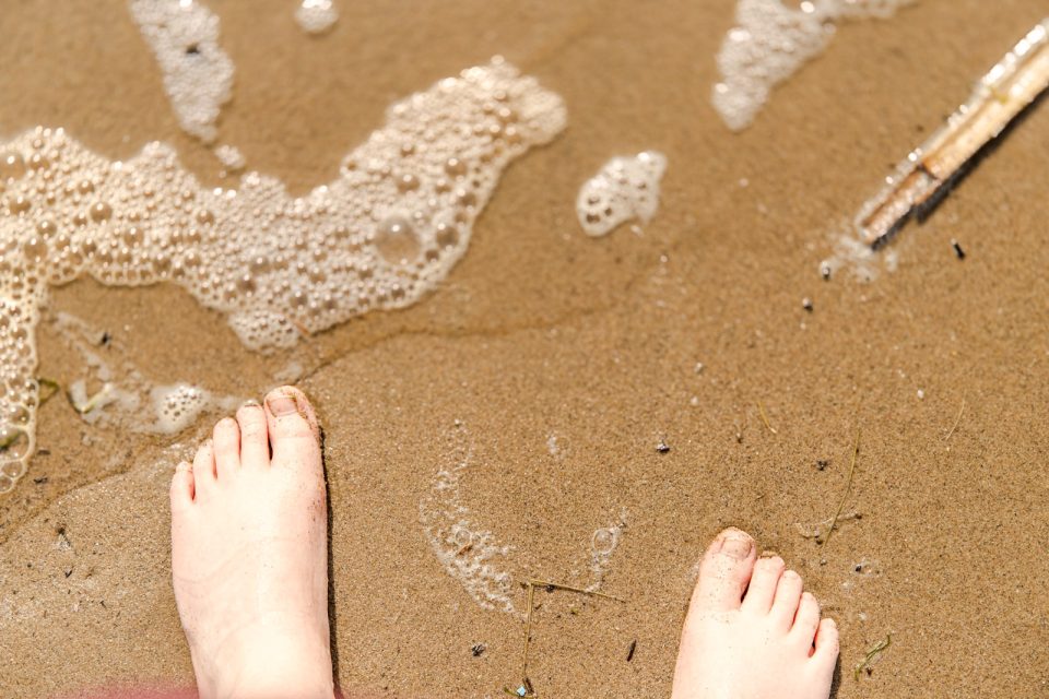 Bare feet on wet sand, with sea foam around them.
