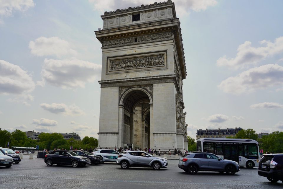 The Arc de Triomphe under a cloudy sky, with traffic circling in front.